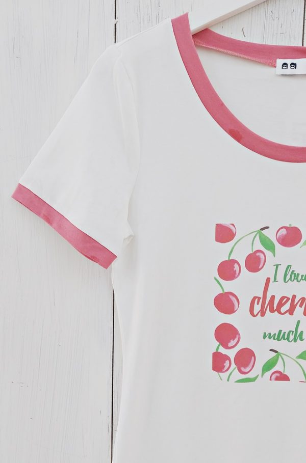 Camiseta blanca Begonia de Lylu de mangas cortas y escote redondo, con estampación de cerezas en el delantero. Detalle de ribetes de cuello y mangas en rosa.