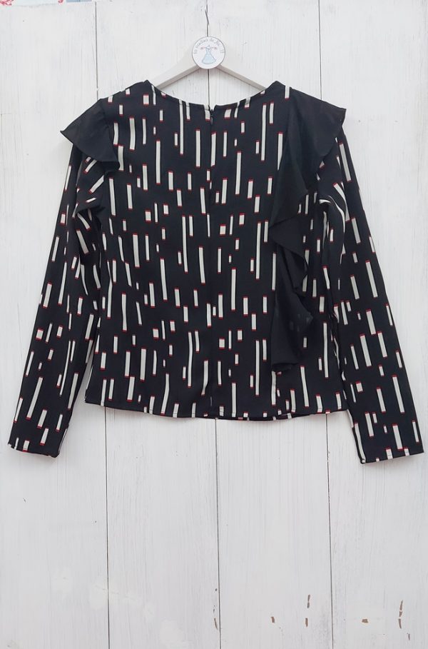 Blusa negra Peoria de Lylu con estampado geométrico en tonos blancos y rojos. Corte recto con volantes decorativos en color negro. Cuello redondo, mangas largas y cierre con cremallera en la espalda.